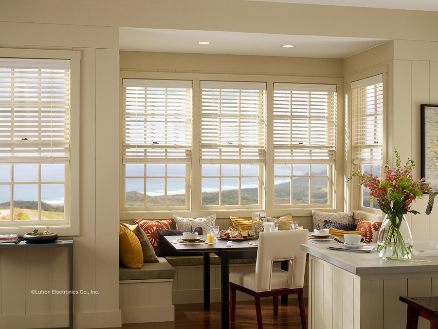 A cozy white kitchen with Lutron wooden blinds on a bay window.