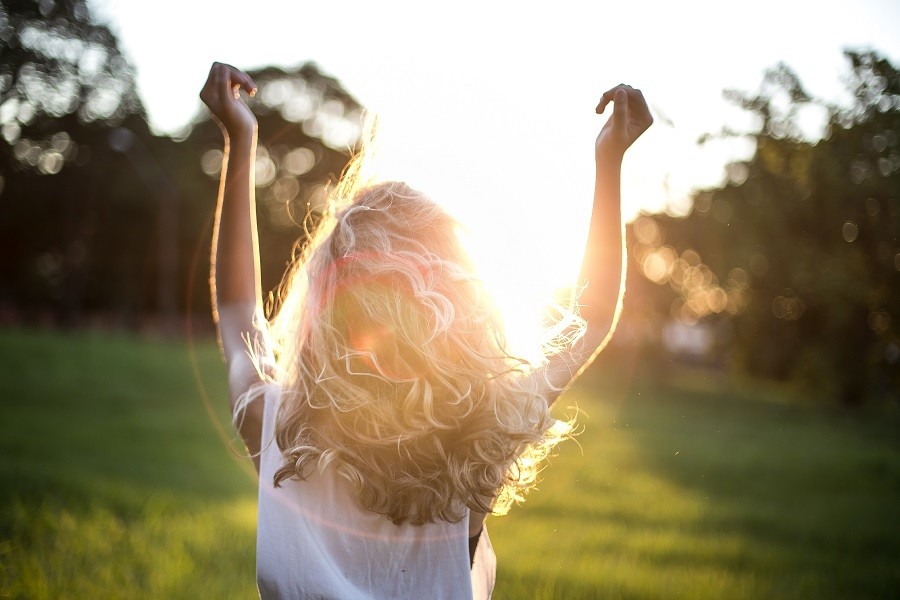 Woman embraces the warmth and life-giving energy of the sun in an open field.