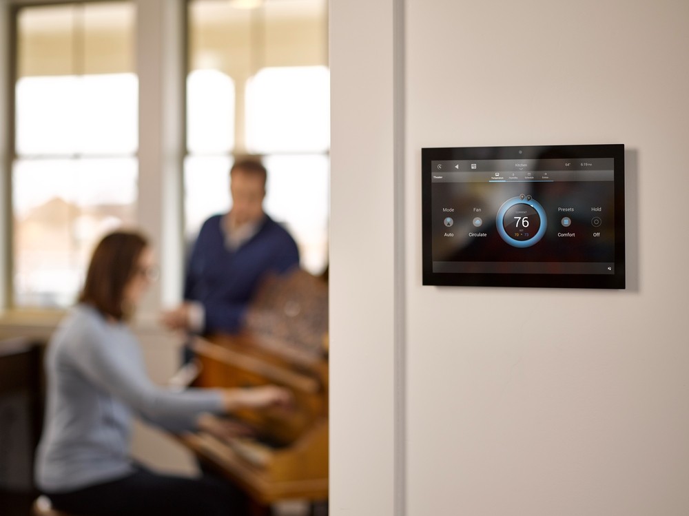 A wall-mounted Control4 tablet with an indoor temperature reading. A couple playing the piano is in the background.