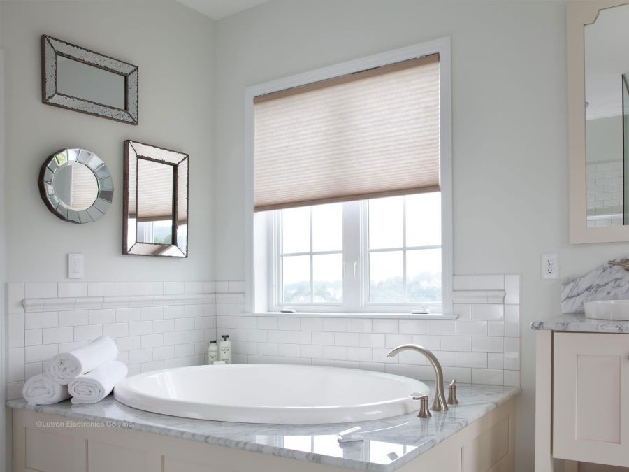 Shades are halfway drawn over a bathroom window above a bathtub.