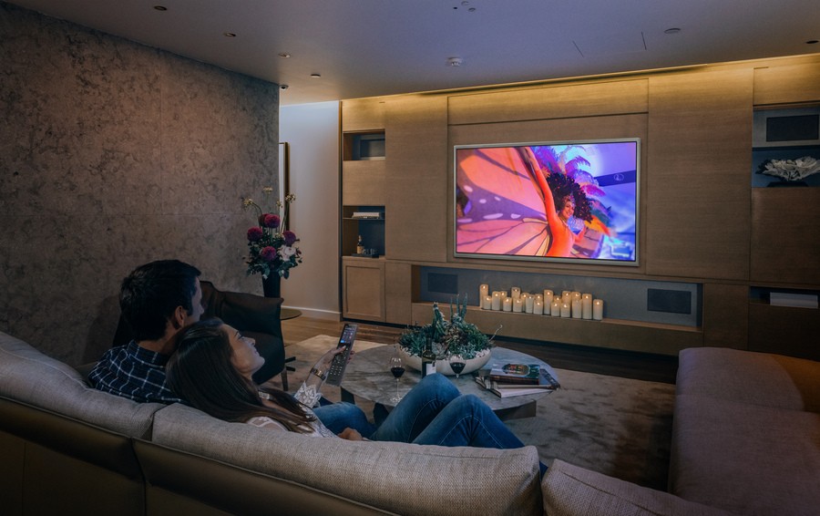 A couple watching TV in a home theater with dim, cozy lights.